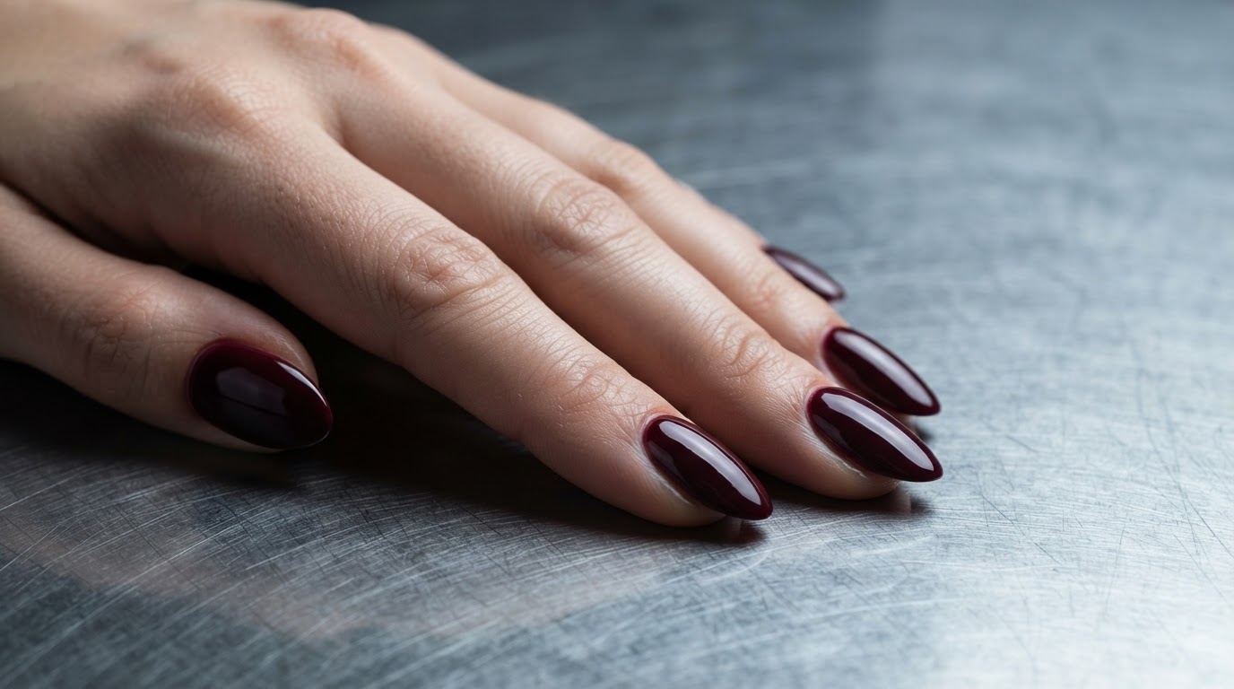 Ruka so štruktúrovanými burgundy nechtami na nerezovej ploche